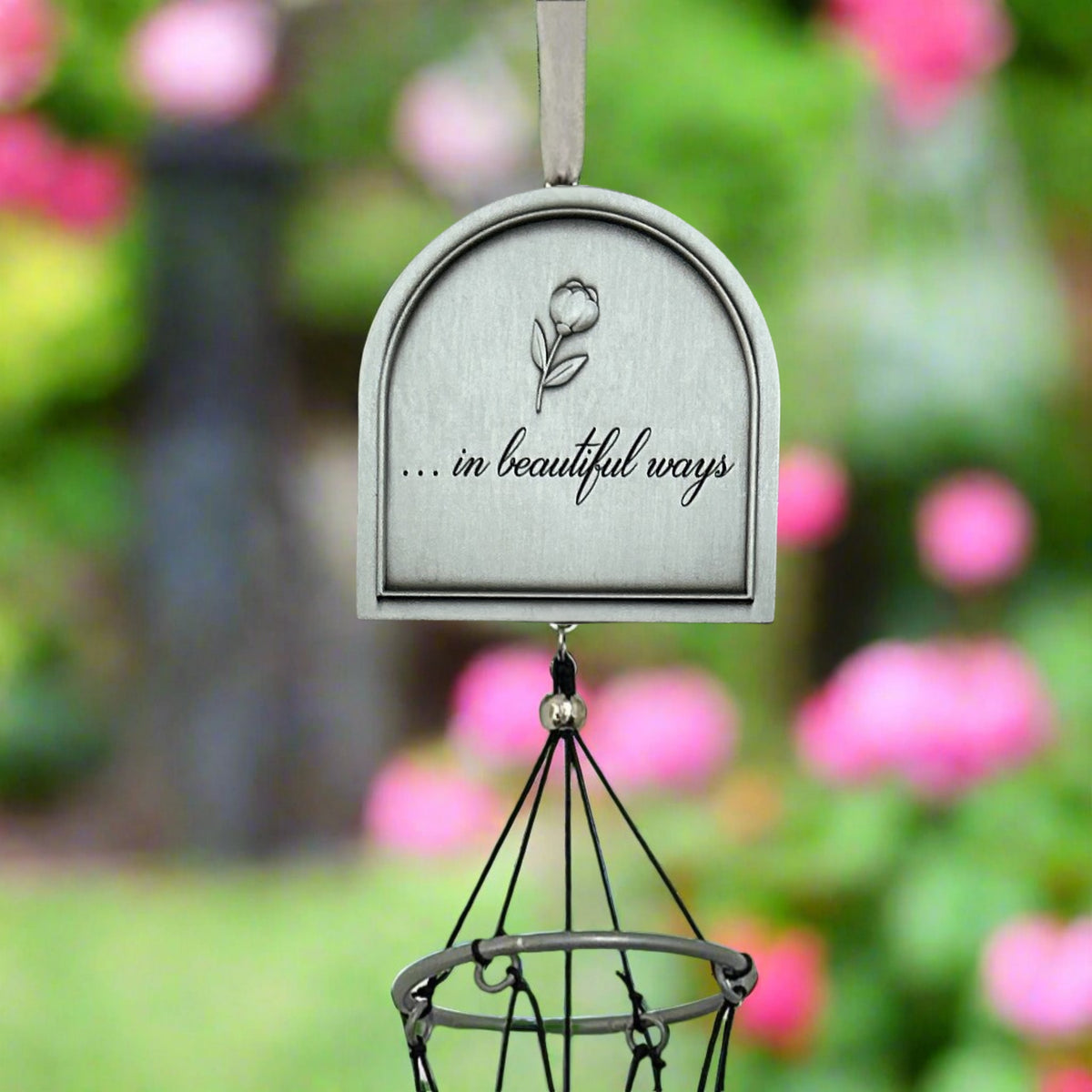 Top of the back of the windchime with &#39;...in beautiful ways&#39; text and flower design against a garden background.
