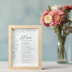 4 of 8:Framed poem titled 'Mom, Now that I'm Older' on a table with flowers in the background.