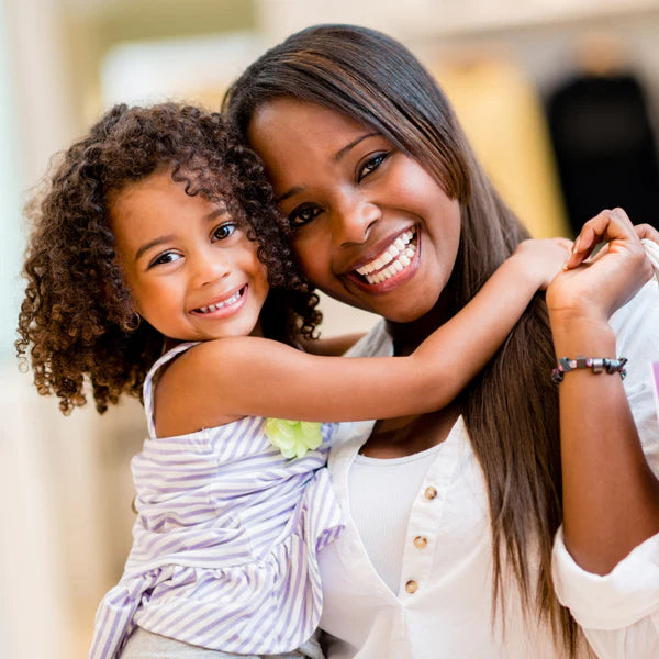 A happy mother and her young daughter smiling and hugging, both looking at the camera - click to shop Mom gifts
