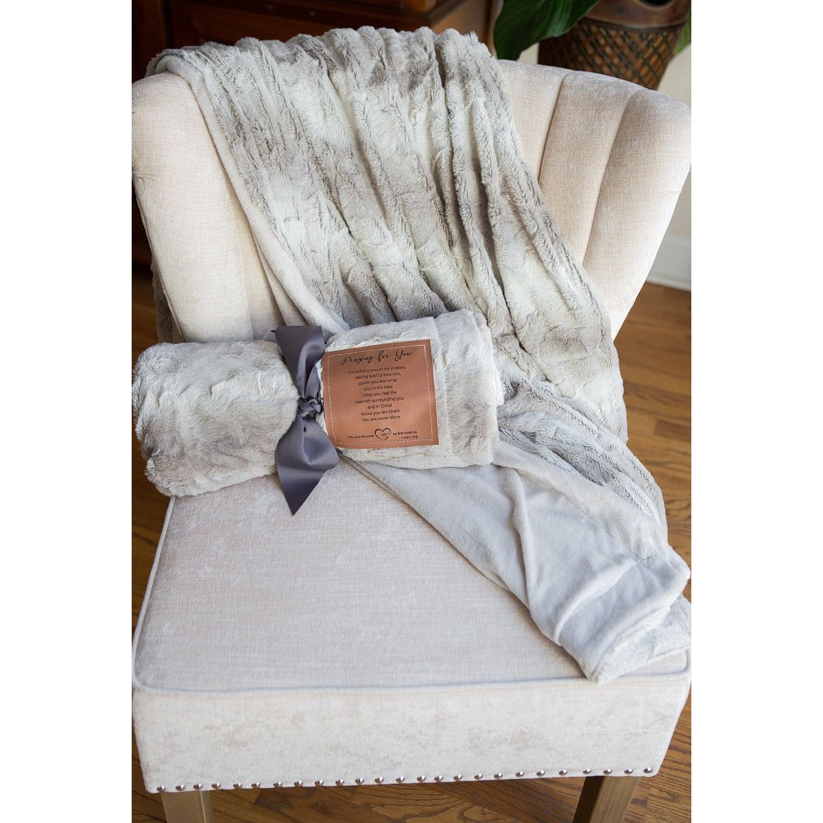 Sympathy blanket rolled and tied with a ribbon on a chair on top of another blanket draped over the chair.