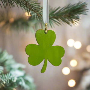 4 of 4:Green glass shamrock ornament hanging from an off-white satin ribbon on a Christmas tree with blurred lights in the background.