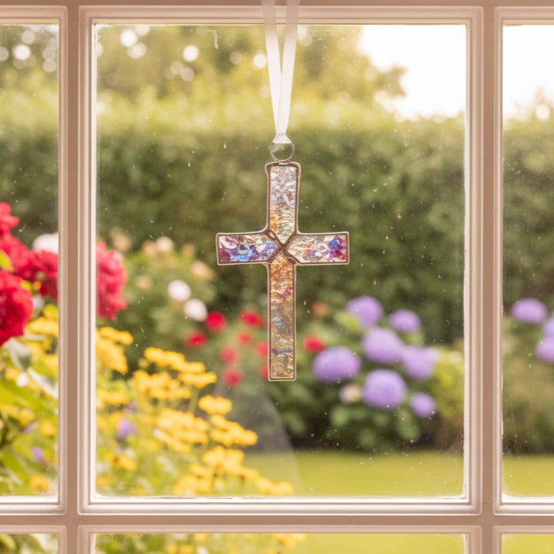 Clear iridescent stained glass cross hanging in a window.