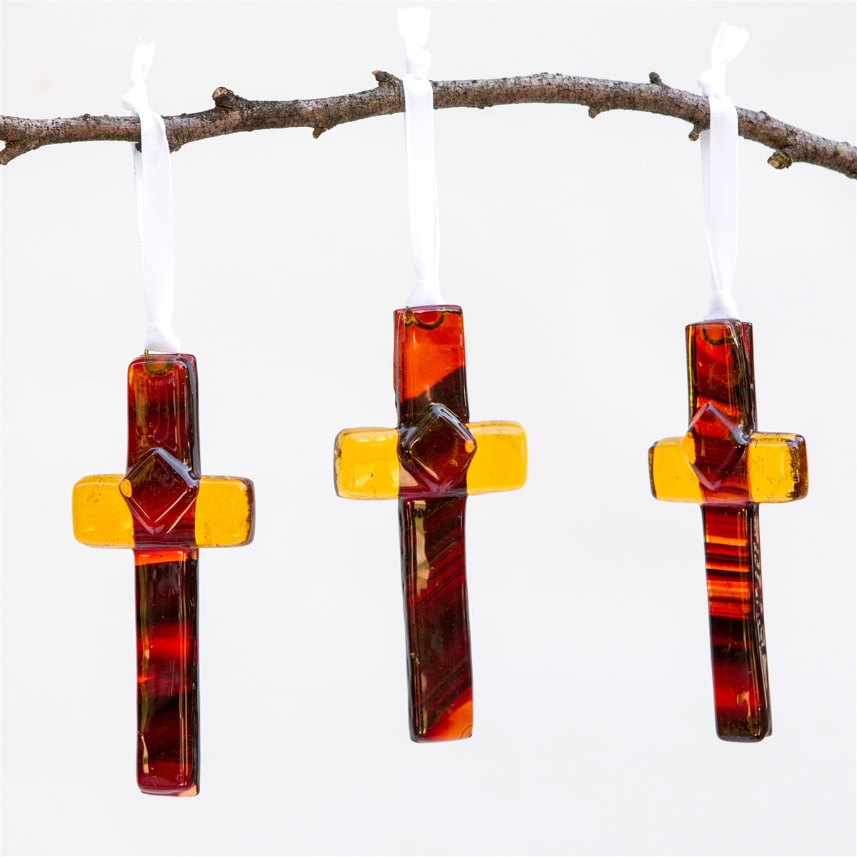 Three amber/brown glass crosses hanging from a branch.