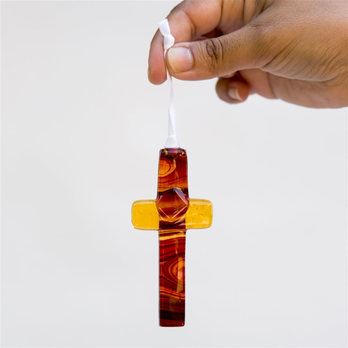 Glass cross being held with the light shining through to show the swirls of amber and brown in the glass