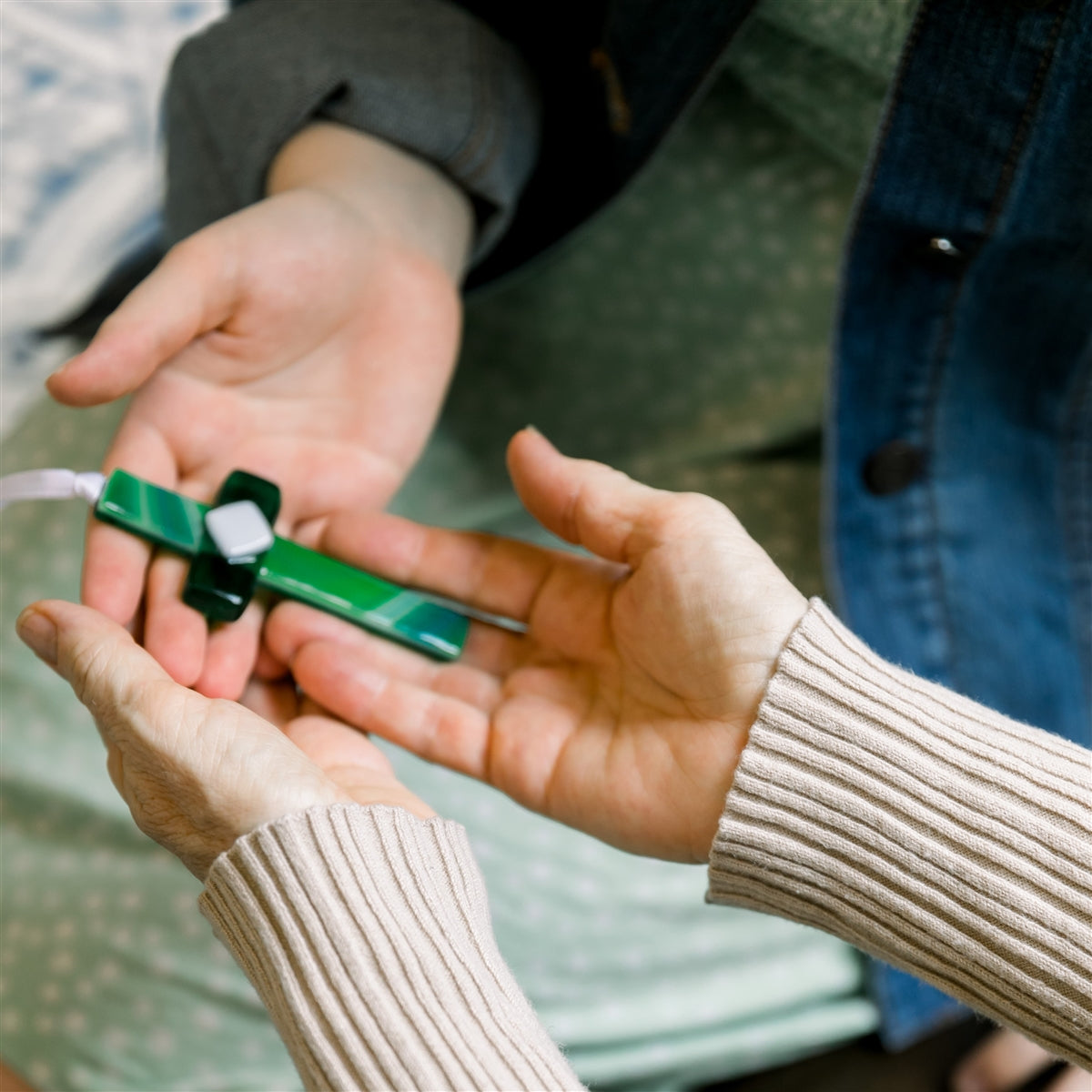 A green glass cross being exchanged between two sets of hands.