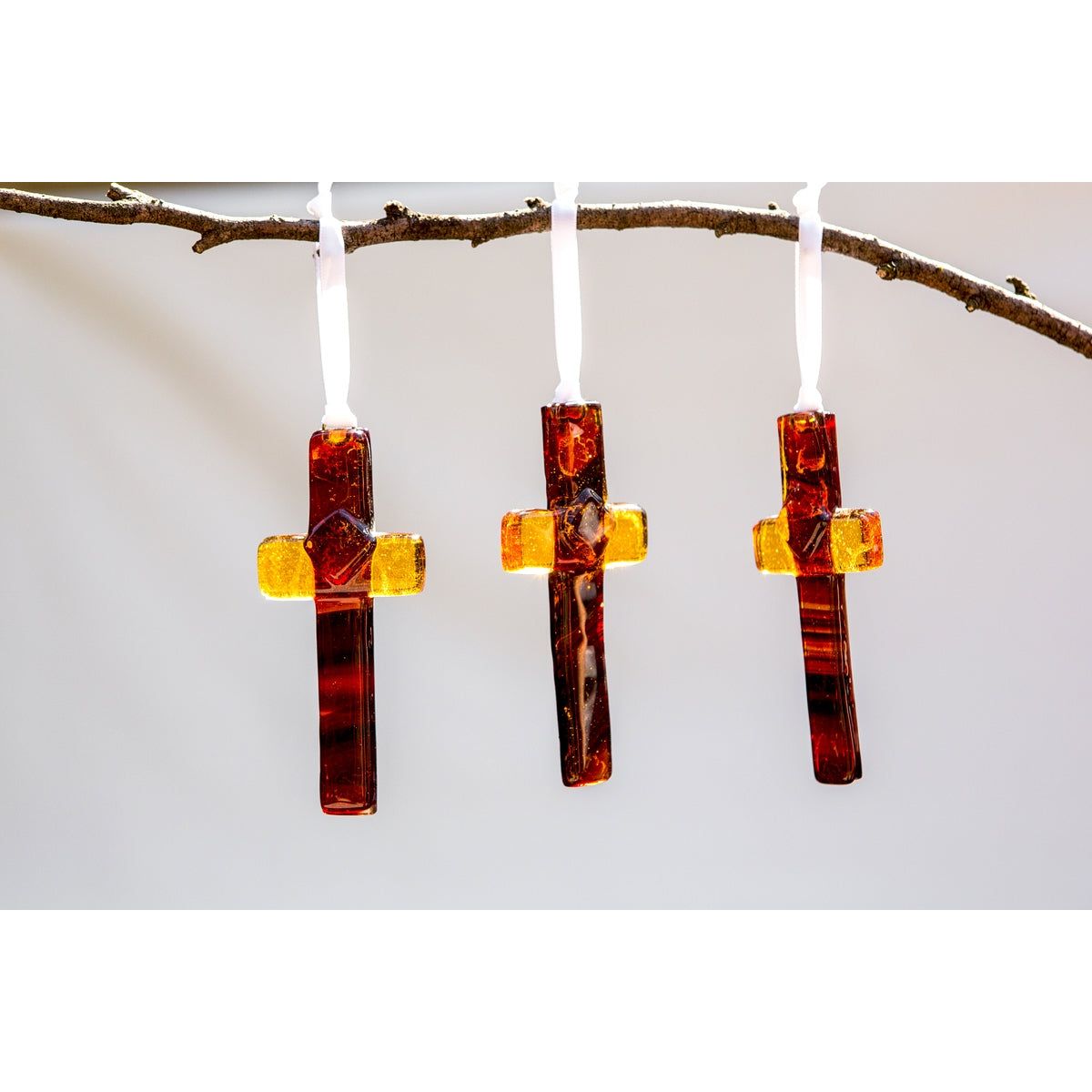 Three amber/brown glass crosses hanging from a branch.