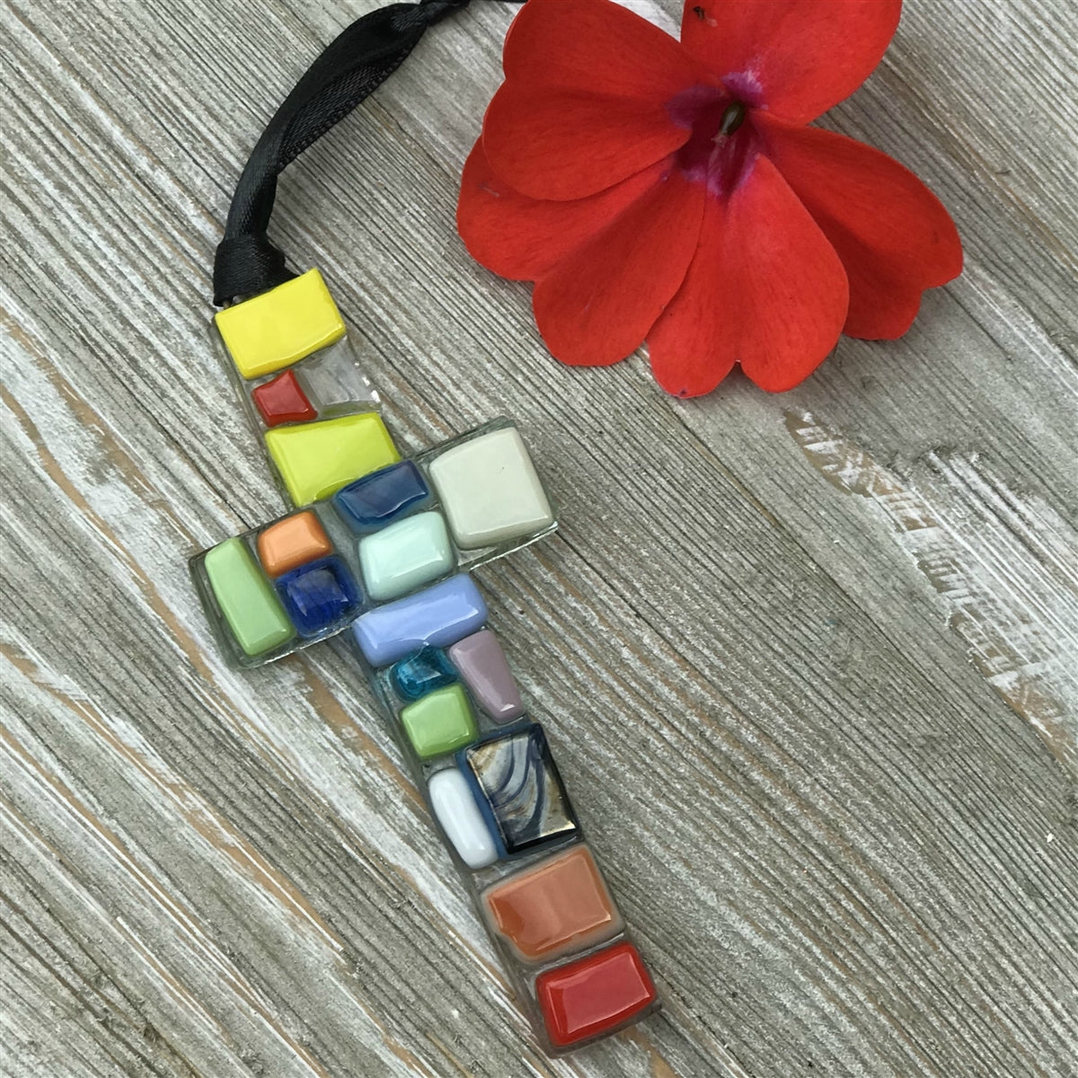 Multicolored mosaic cross with black satin ribbon for hanging.