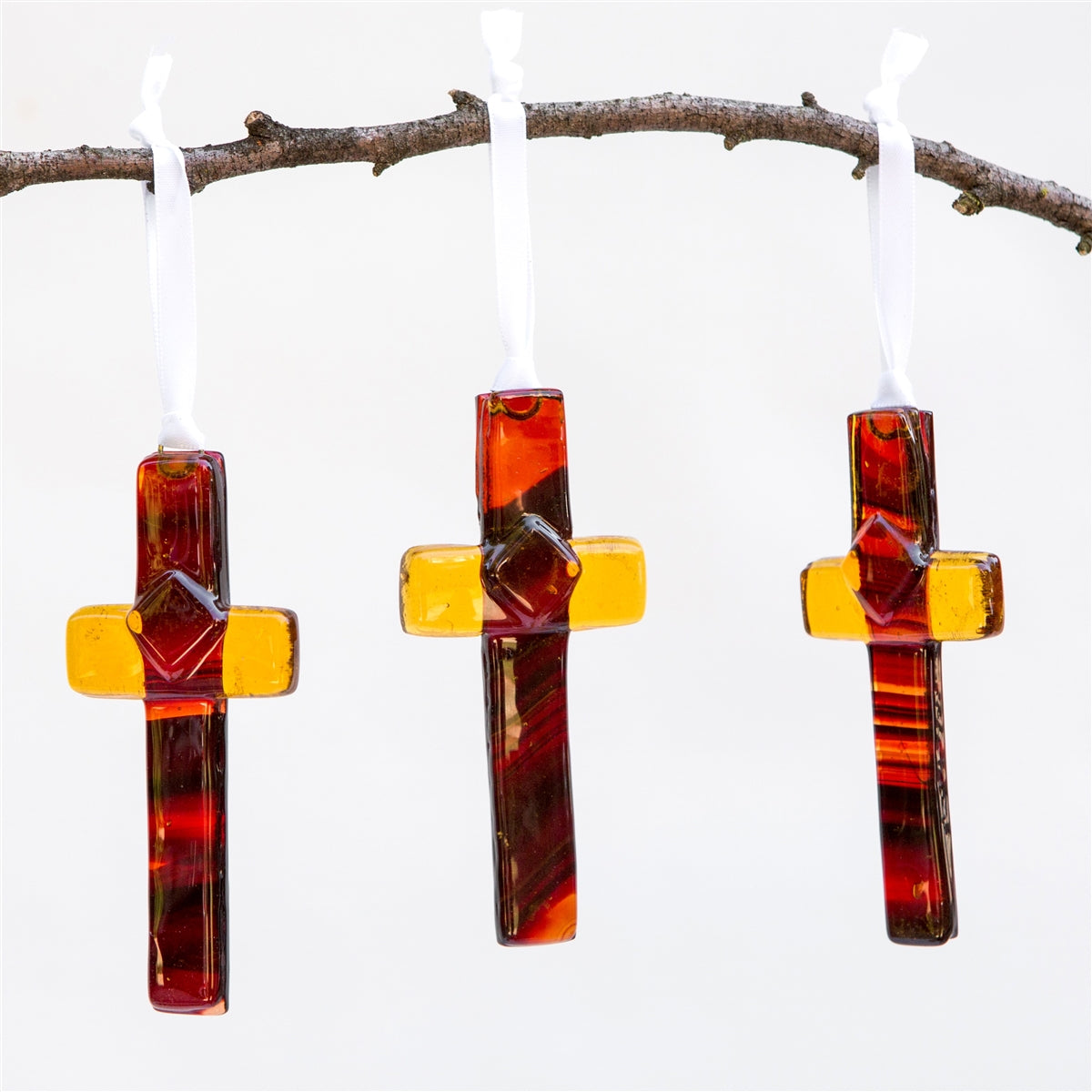 Three amber/brown glass crosses hanging from a branch.