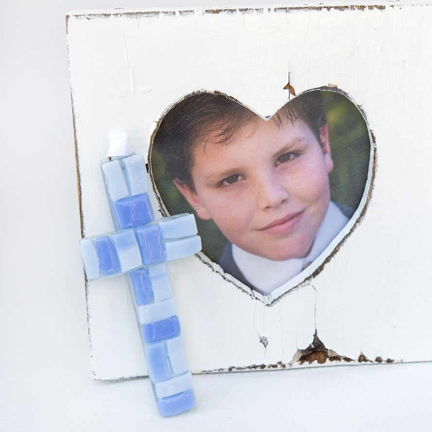 A blue mosaic cross with white satin ribbon for hanging.