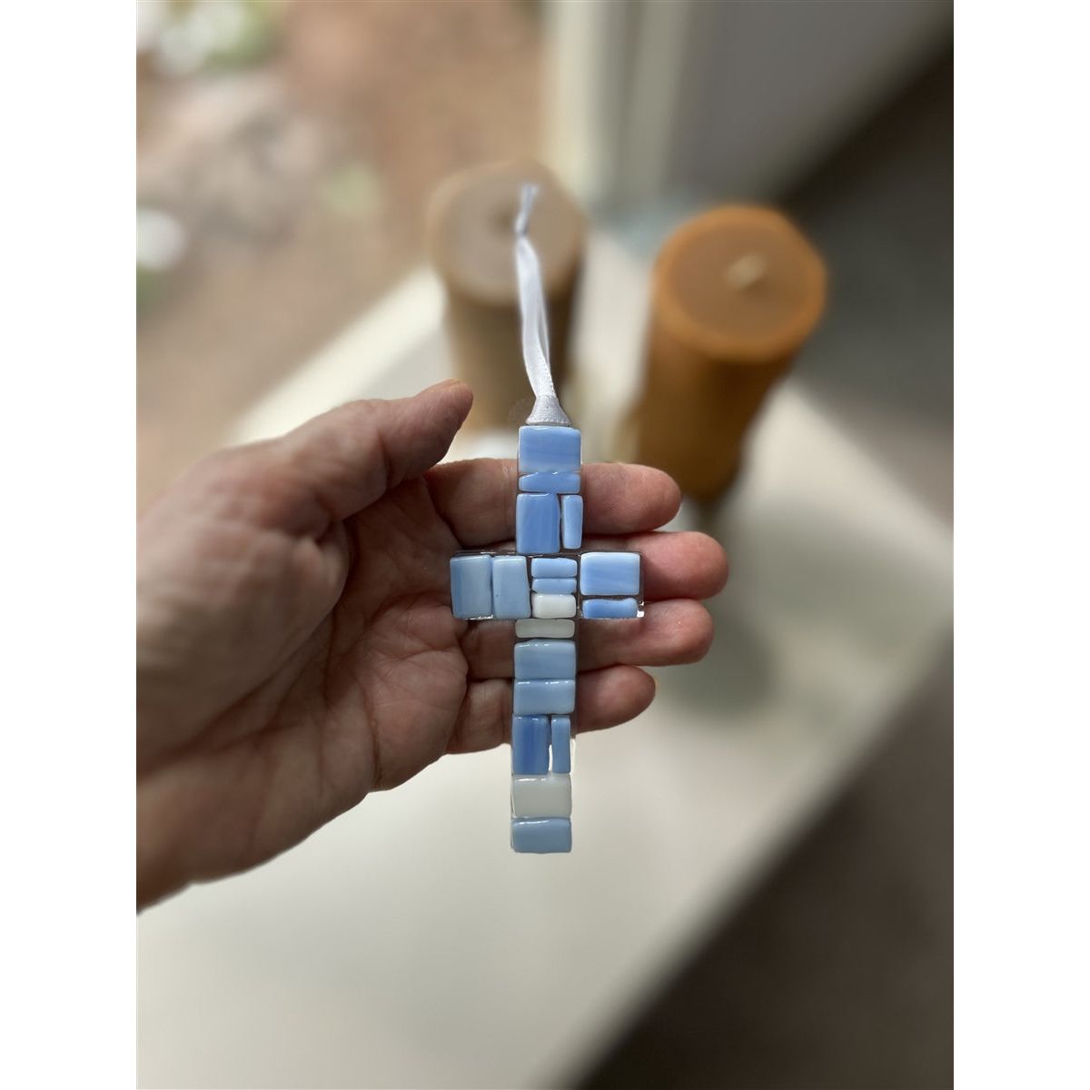 A blue mosaic cross being held in a hand.