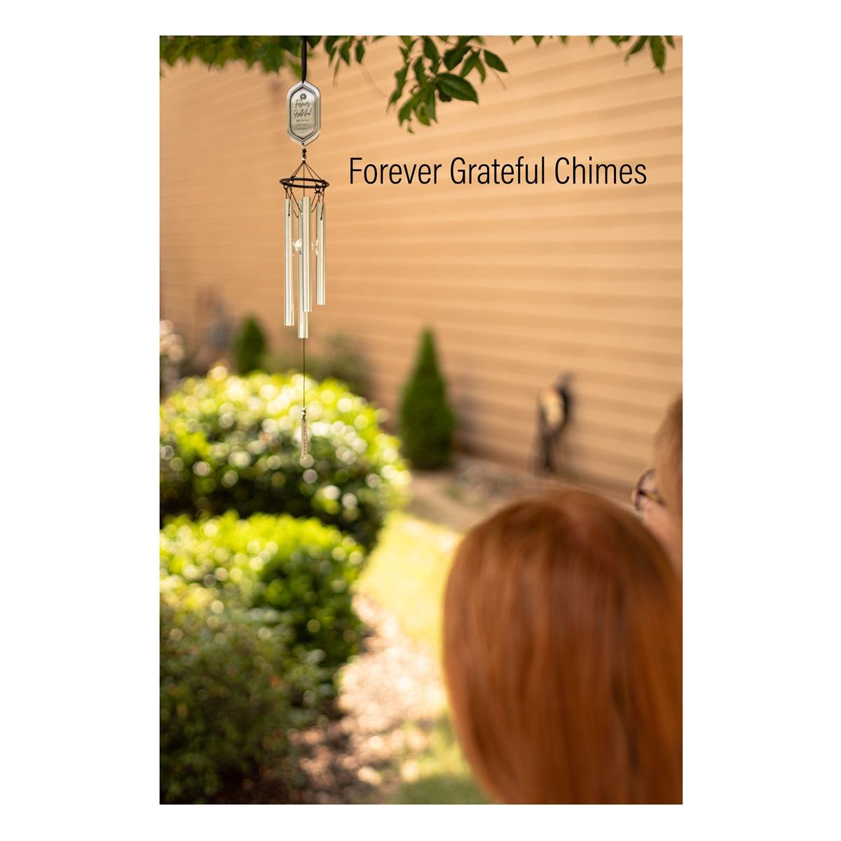 Two women admiring the windchime hanging in a tree.