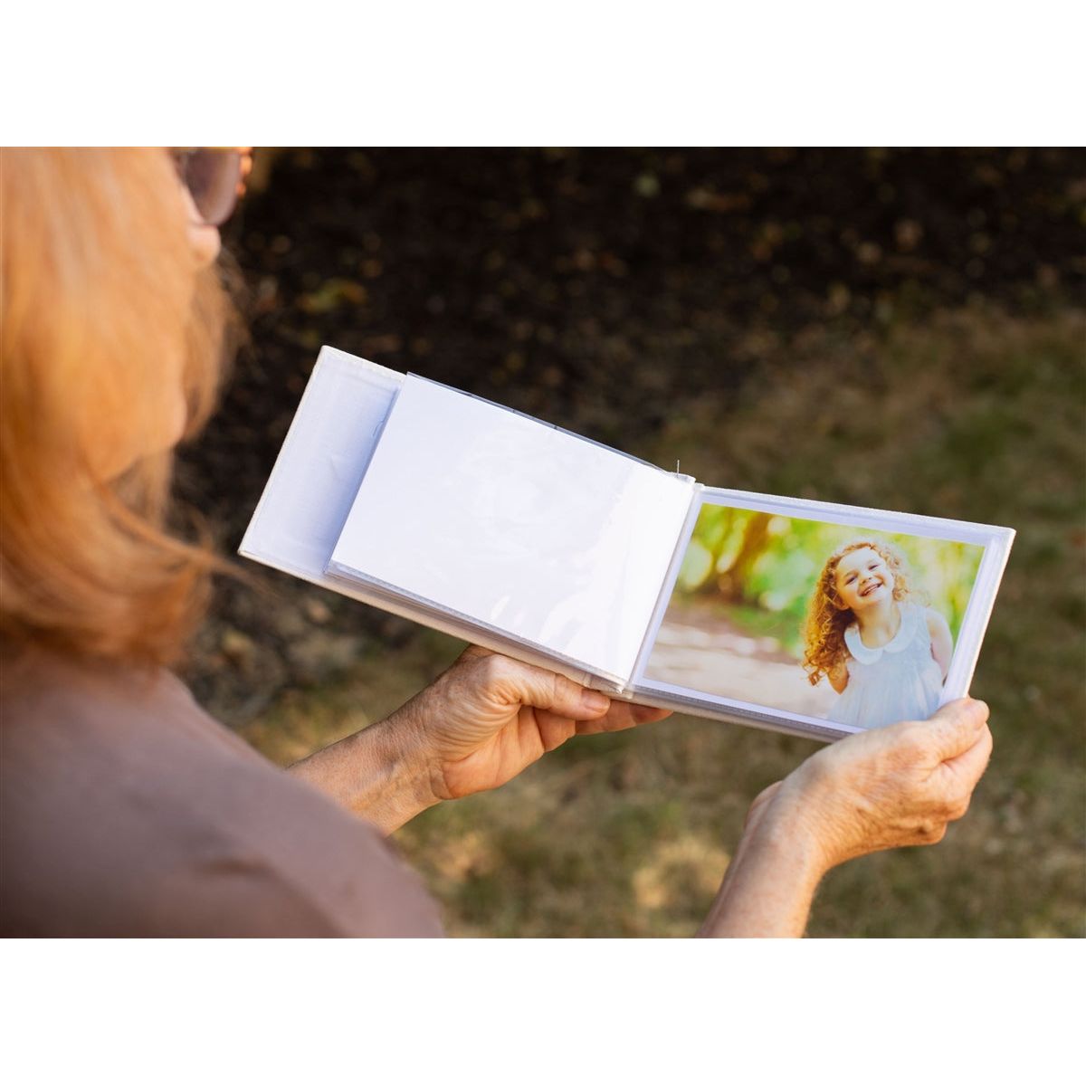 Open photo album being held in hands showing photos in the plastic sleeve.